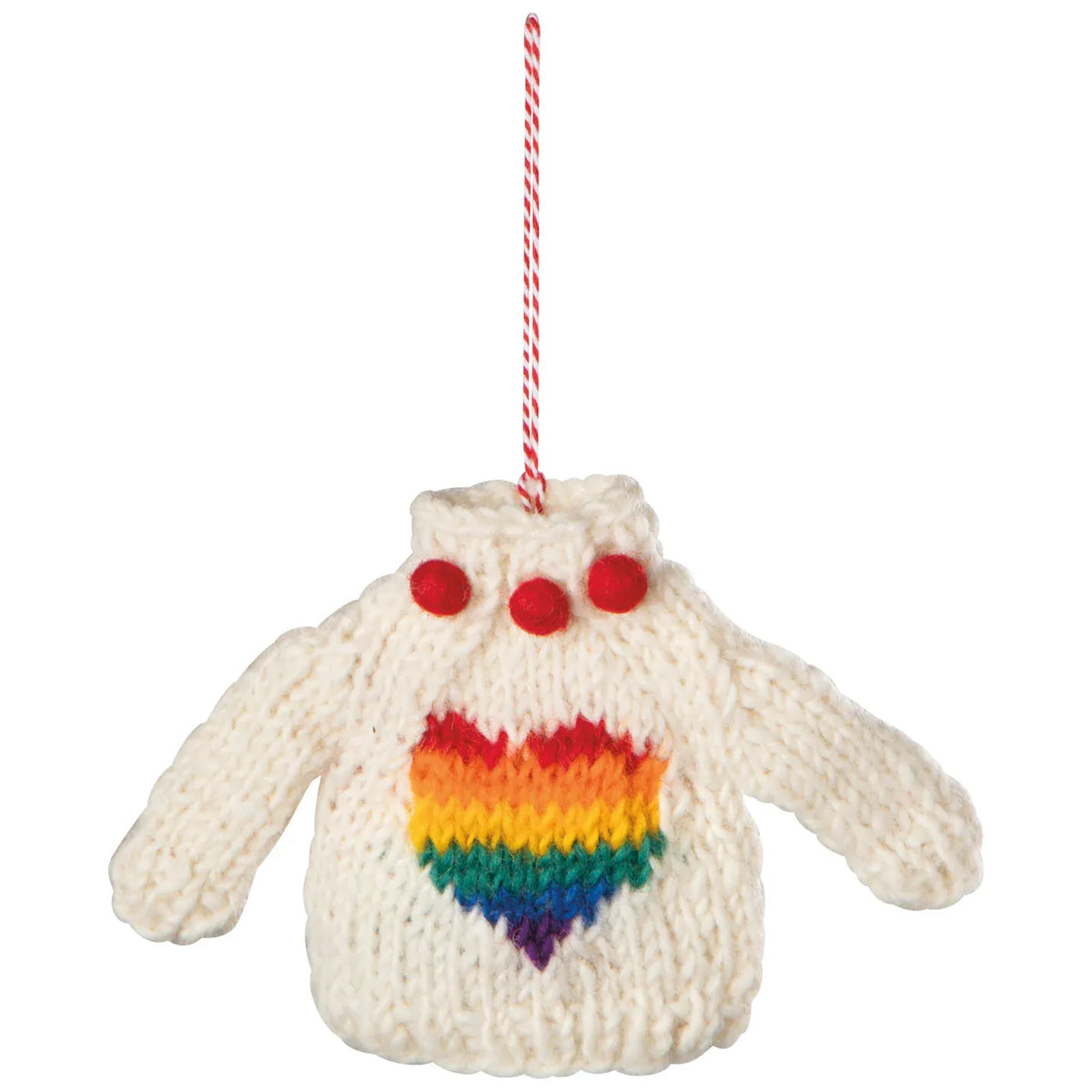 A knitted Christmas ornament shaped like a cream-colored sweater with a rainbow heart.